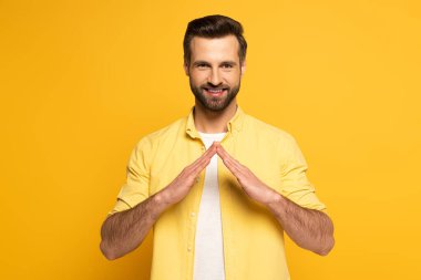Gülümseyen adam sarı arka planda işaret diliyle kelime evini gösteriyor.