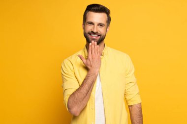 Gülümseyen adam kameraya bakarken işaret diliyle konuşan kelimeyi sarı arka planda gösteriyor.