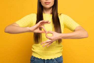 Cropped view of woman showing interpretation sign in deaf and dumb language on yellow background