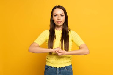 Young woman showing marriage sign in deaf and dumb language on yellow background