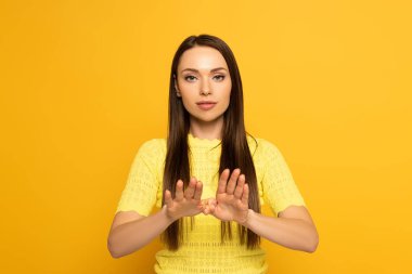 Beautiful woman showing sign in deaf and dumb language on yellow background