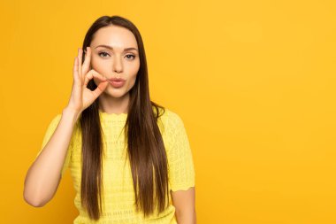 Woman with hand near mouth showing sign from deaf and dumb language on yellow background