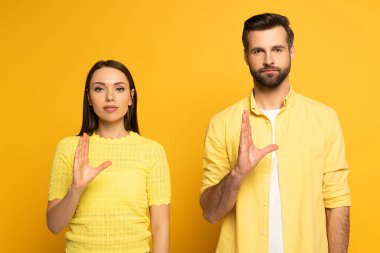 Sarı arka planda işaret diliyle hareket eden genç çift.