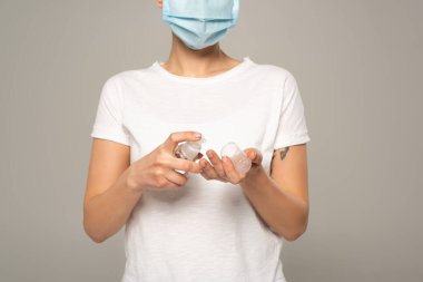 Griye izole edilmiş el dezenfektanı kullanan tıbbi maskeli kadın görüntüsü. 