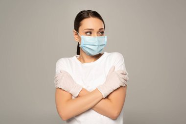 Tıbbi maskeli ve lateks eldivenli genç bir kadın griye bakıyor. 