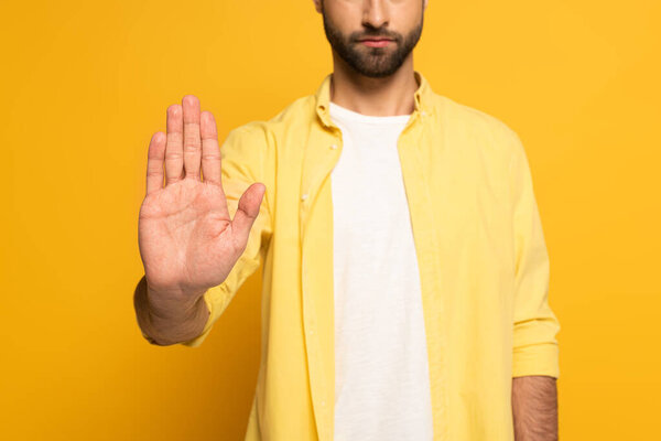 Cropped view of man showing stop sign on yellow background