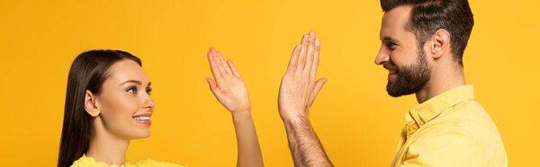 Side view of smiling couple high five isolated on yellow, panoramic shot 