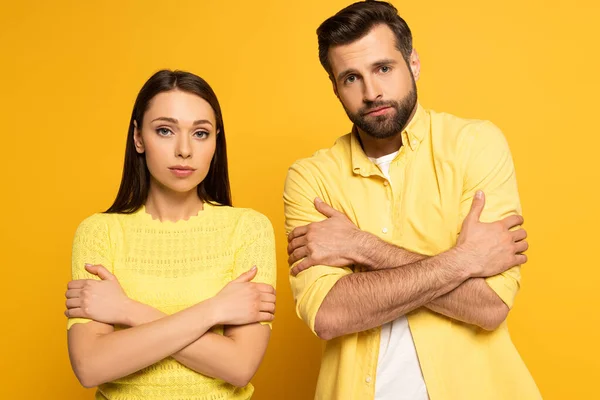 年轻夫妇交叉双臂望着黄色背景的相机 — 图库照片