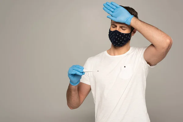 Mężczyzna Masce Ochronnej Rękawiczkach Lateksowych Trzymający Termometr Dotykające Czoło Izolowane — Zdjęcie stockowe