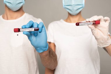 Tıbbi maskeli, lateks eldivenli, üzerinde kan örnekleri olan test tüpleri ve gri harfleri olan koronavirüs yazan çift görüntüsü. 