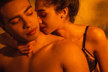 Tutkulu Afrikalı Amerikalı kadın. Gözleri kapalı, erkek arkadaşına sarılıyor.