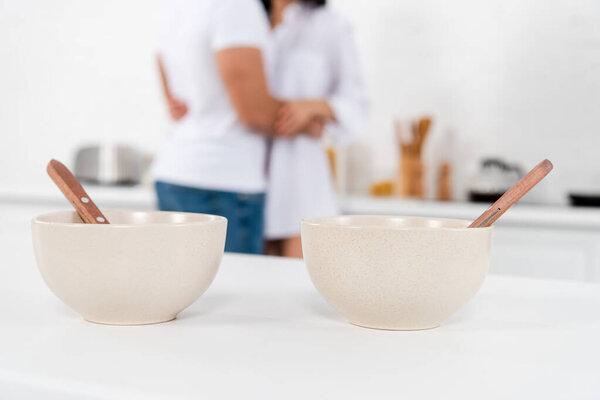 Cropped view of couple hugging near bowls with spoons on table in kitchen