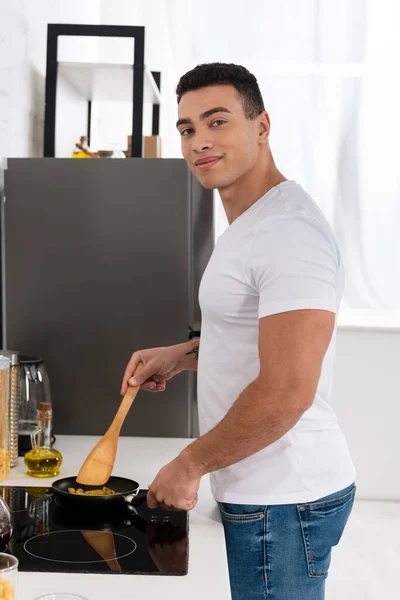 Чоловік Посміхається Дивлячись Камеру Готуючи Сковородою Шпателем Біля Кухонної Плити — стокове фото