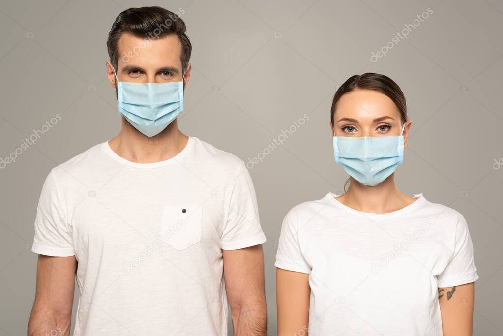 Young couple in medical masks looking at camera isolated on grey 