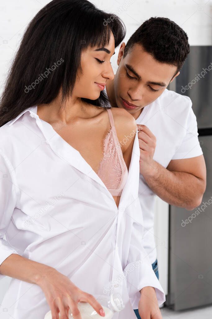 Man kissing african american woman with bottle of milk in kitchen