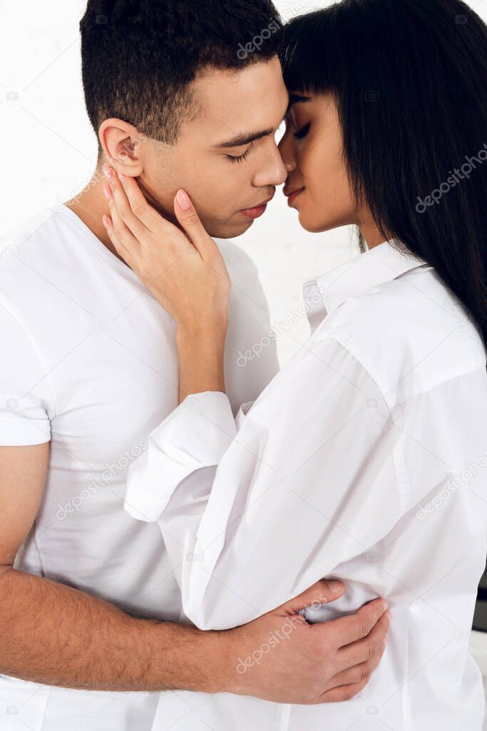 Interracial couple hugging and kissing on white background