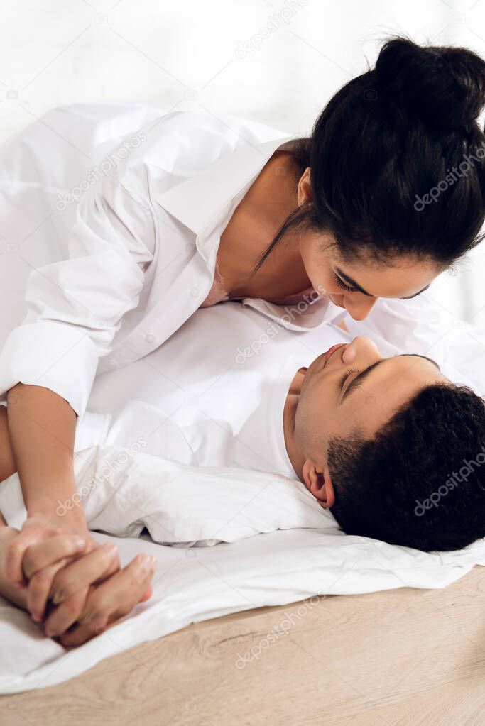 Interracial couple with clenched hands lying on bed in bedroom
