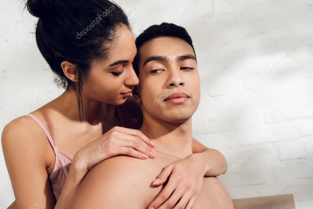 African american woman hugging boyfriend from behind in bedroom