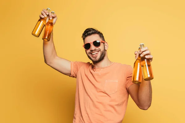 戴着太阳镜快乐的年轻人拿着啤酒瓶 在黄色的背景上对着相机微笑 — 图库照片