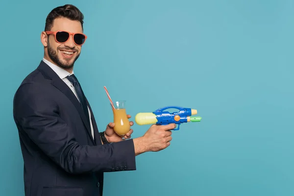 Empresário Alegre Segurando Arma Água Vidro Suco Laranja Isolado Azul — Fotografia de Stock