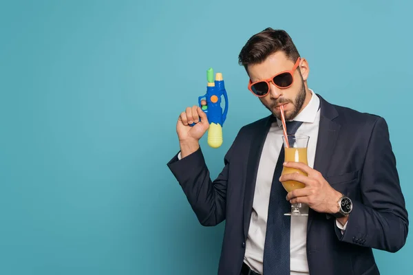 Zelfverzekerde Zakenman Zonnebril Drinken Sinaasappelsap Houden Waterpistool Blauwe Achtergrond — Stockfoto