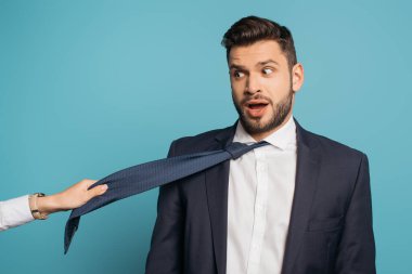 Mavi arka planda, şaşırmış iş adamının kravatını çeken kadının kısmi görüntüsü