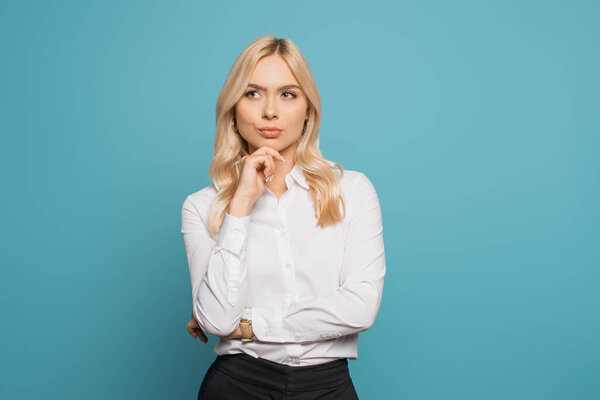 pensive businesswoman holding hand near chin while looking away on blue background