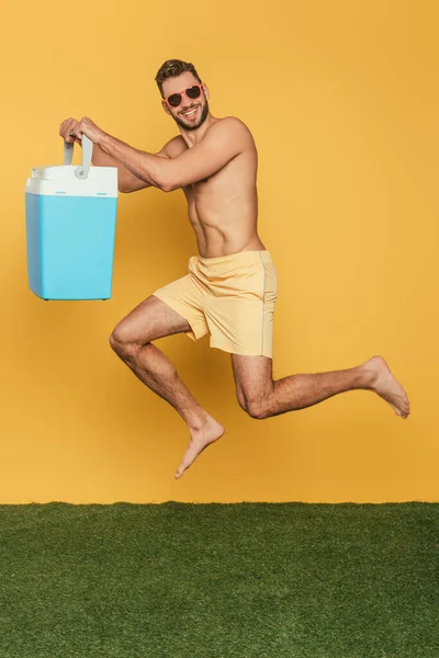 Smiling Shirtless Man Holding Portable Fridge While Levitating Yellow Background — Stock Photo, Image