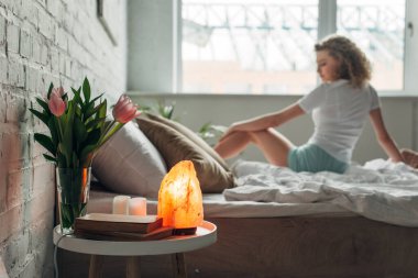 Güzel kız yatakta Himalaya tuz lambasıyla, çiçekler ve kitaplar yatak odasında, seçici bir odak