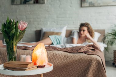 Himalaya tuz lambası, çiçekler ve kitaplarla yatak odasında dinlenen kızın seçici odağı