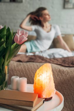 Himalaya tuz lambası, laleler, mumlar ve kitaplarla yatak odasındaki seçici kadın.