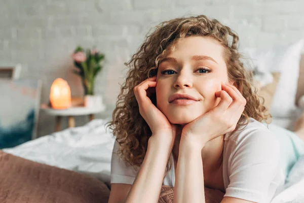 curly girl in homewear lying on bed in bedroom with Himalayan salt lamp