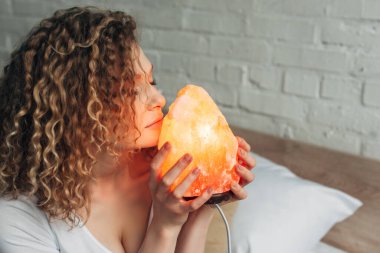 İç çamaşırlı kıvırcık kız yatak odasında Himalaya tuzlu lambasını tutuyor.