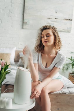 attractive girl sitting in bedroom with air purifier and tulip flowers clipart