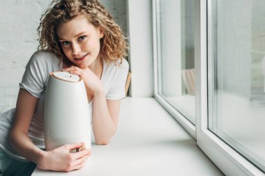 beautiful happy girl with air purifier on windowsill clipart