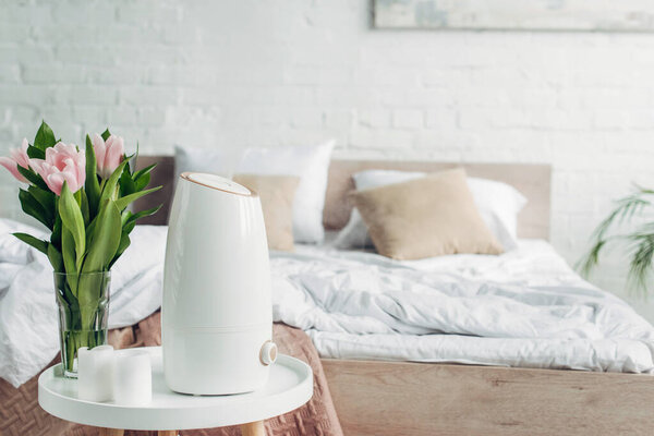 white ultrasonic purifier, tulips and candles on table in bedroom 
