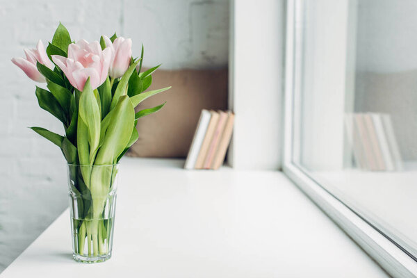 bouquet of pink tulips in glass on windowsill with books