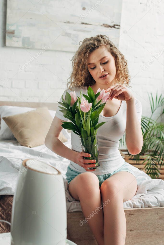 curly girl holding tulip flowers while sitting in bedroom with air purifier 