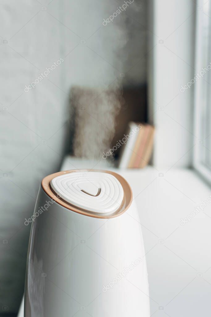 humidifier spreading steam and standing on windowsill at home