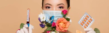 panoramic shot of asian girl in latex gloves and floral face mask with butterfly holding pills and coronavirus blood test isolated on beige clipart