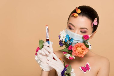attractive nude asian girl in latex gloves and floral face mask with butterflies holding coronavirus blood test isolated on beige clipart