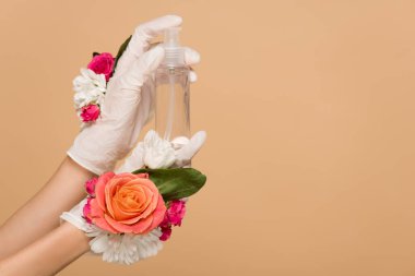 cropped view of woman in floral latex gloves holding antiseptic spray isolated on beige clipart