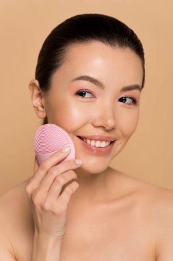 Çekici, çıplak Asyalı kız pembe silikon temizleyici yüz fırçası kullanıyor.