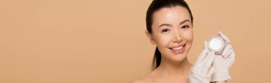 Plastik eldivenli gülümseyen çıplak Asyalı kızın panoramik görüntüsü. Elinde bej rengi kremi olan cam bir kap var.
