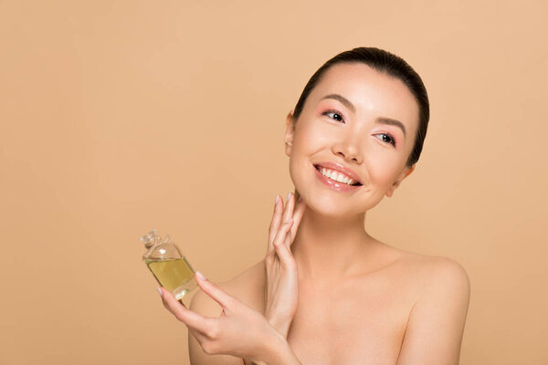 beautiful smiling naked asian girl applying perfume on skin isolated on beige