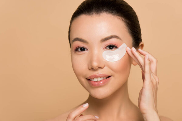 beautiful smiling asian girl with collagen eye pads isolated on beige