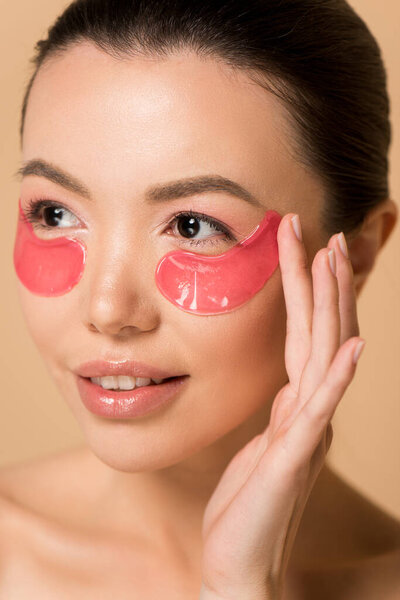 attractive tender asian woman with pink collagen eye pads isolated on beige