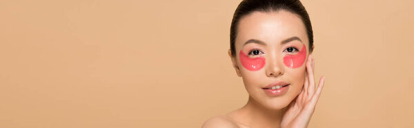 panoramic shot of tender asian woman with pink collagen eye pads isolated on beige
