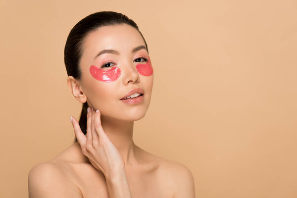 beautiful tender nude asian woman with pink collagen eye pads isolated on beige