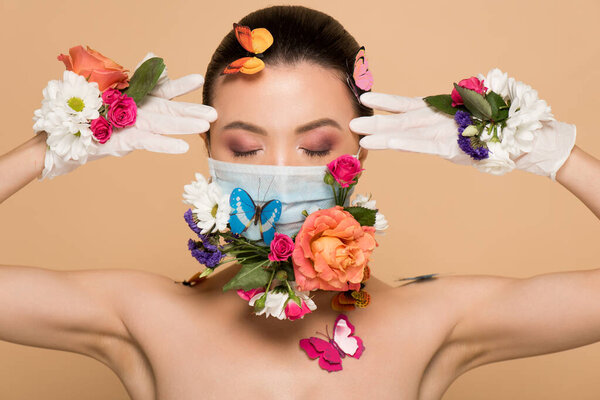 attractive asian woman with closed eyes in latex gloves and floral face mask with butterflies isolated on beige